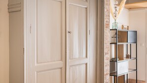 Un couloir avec des portes blanches, une étagère en métal noir et un vase contenant des fleurs séchées.