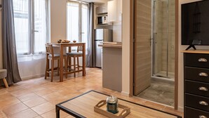 Une cuisine moderne équipée d’un four à micro-ondes, d’un réfrigérateur et de meubles de rangement en bois. On y trouve également un coin repas avec une table et des chaises, ainsi qu’une porte de douche en verre.