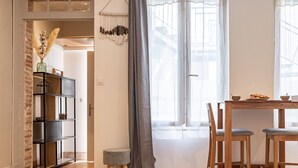 Un coin repas comprenant une table et des chaises en bois, un petit tabouret et une étagère où sont disposés des objets décoratifs.