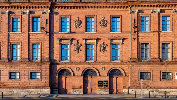 Un bâtiment en briques rouges, doté de nombreuses fenêtres, d’arches décoratives et d’un balcon.