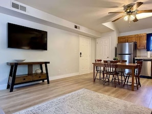 A modern kitchen with a dining area, a flat-screen TV, and a ceiling fan.