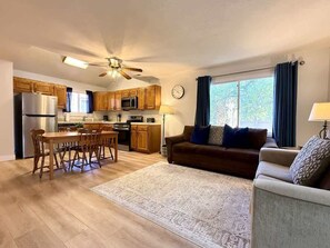 A spacious living area with a wooden dining table, a sofa, and a kitchen in the background.