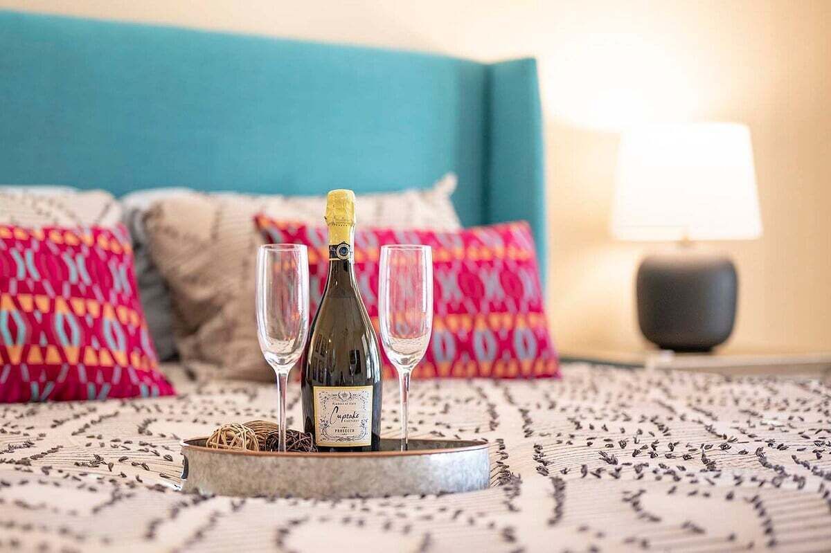 A bed with a patterned bedspread, a bottle of champagne, and two glasses on a tray.