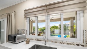 A modern kitchen with a stainless steel sink, a microwave, and a view of a swimming pool through large windows.