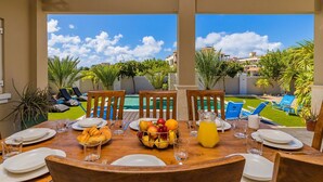 A dining table set for breakfast with a view of a pool and greenery.