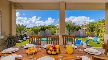 A dining table set for breakfast with a view of a pool and greenery.