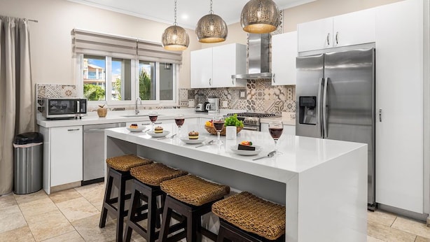 A modern kitchen with white cabinetry, a stainless steel refrigerator, and a central island with bar stools.
