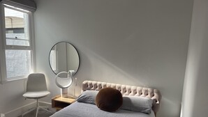 A bedroom with a bed, a chair, a round mirror, and a window.