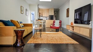 A modern living room with a sofa, coffee table, and a red chair. There is a kitchen area with cabinets and a refrigerator.