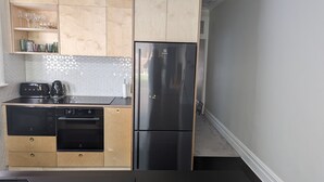 A compact kitchen with a stainless steel refrigerator, a toaster, a kettle, and a dishwasher.