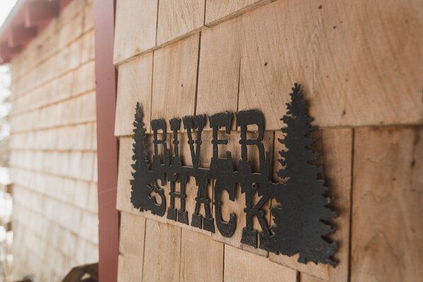 Un cartello di legno con la scritta 'River Shack' e sagome di alberi.
