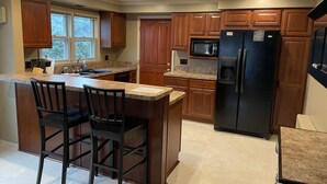 Una cocina con armarios de madera, un refrigerador negro, un microondas y una encimera de granito.