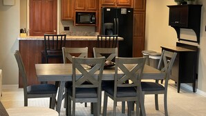 Cocina moderna con armarios de madera, un microondas integrado y un refrigerador. Hay una mesa de comedor con seis sillas y una pequeña isla con un lavaplatos.