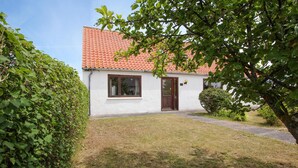 Ein kleines, eingeschossiges Haus mit roten Ziegeln, weissen Wänden und einer Haustür.