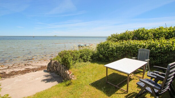 Eine Strandlage mit Tisch und Stühlen, einer Steinmauer und Blick auf das Meer.