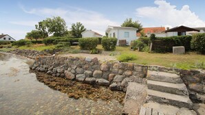 Ein Küstenanwesen mit einer Steinmauer, die Strand und Gebäude trennt, klarem Wasser und einer Rasenfläche mit einer Bank.