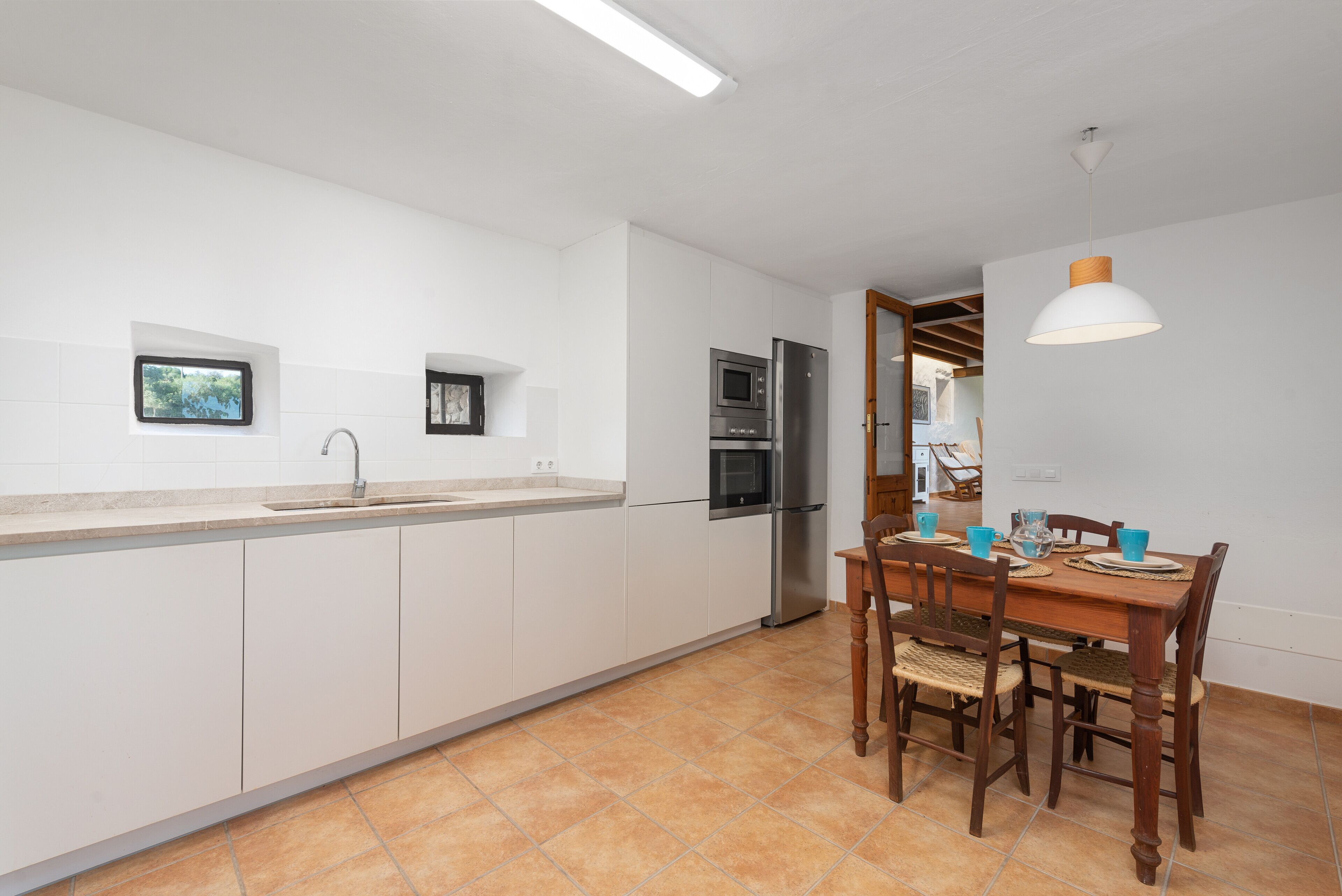 A kitchen with white cabinets, a stainless steel refrigerator, and a dining area with a wooden table and chairs.