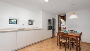 A kitchen with white cabinets, a stainless steel refrigerator, and a dining area with a wooden table and chairs.