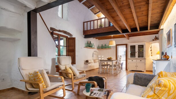 Un'ampia zona giorno con soffitto alto, travi in legno e un balcone. Sono disponibili diversi posti a sedere, tra cui un divano, sedie e una poltrona a dondolo. Si nota anche un tavolo da pranzo e sedie.