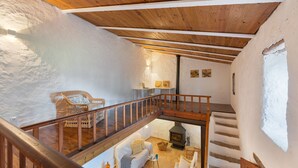 Un'atmosfera rustica con una scala in legno, una poltrona in vimini, un divano bianco e un camino.