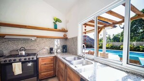 Een moderne keuken met granieten werkbladen, houten kasten en een groot raam met uitzicht op een zwembad.