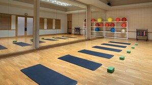 A spacious room with wooden flooring, large mirrors, and exercise mats arranged for stretching.