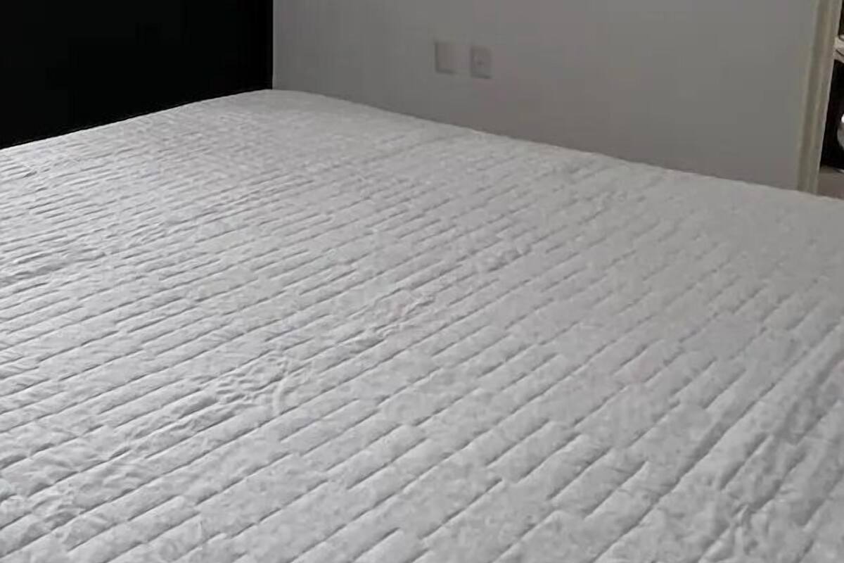 Una habitación con una cama, una puerta oscura y una pared de color claro con dos interruptores.