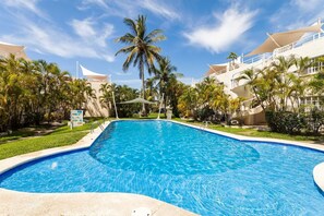 A swimming pool surrounded by palm trees and a white building with a curved roof. - Condos Mar PD  (Acapulco)