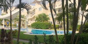 Una piscina rodeada de palmeras y un edificio de varios pisos con balcones.