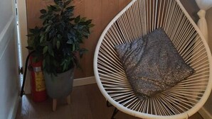 Una habitación con una pared de madera, una silla blanca con cojín, una planta en maceta y tres cuadros enmarcados.