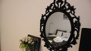 Un dormitorio con un espejo grande y ornamentado, una mesita de noche con un florero y un cartel con frases románticas.