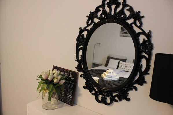 A bedroom with a large ornate mirror, a bedside table with a vase of flowers, and a sign with romantic phrases.