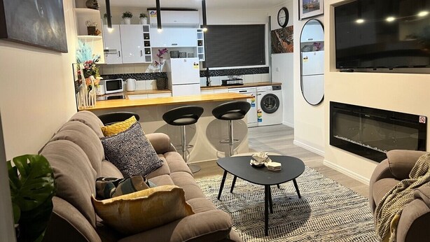 A modern living room with a sofa, coffee table, and a TV. There is a kitchen area with a fridge, microwave, and sink. - Newly Listed and Centrally located , walk to restaurant's , cafes and shopping , (Boondall)