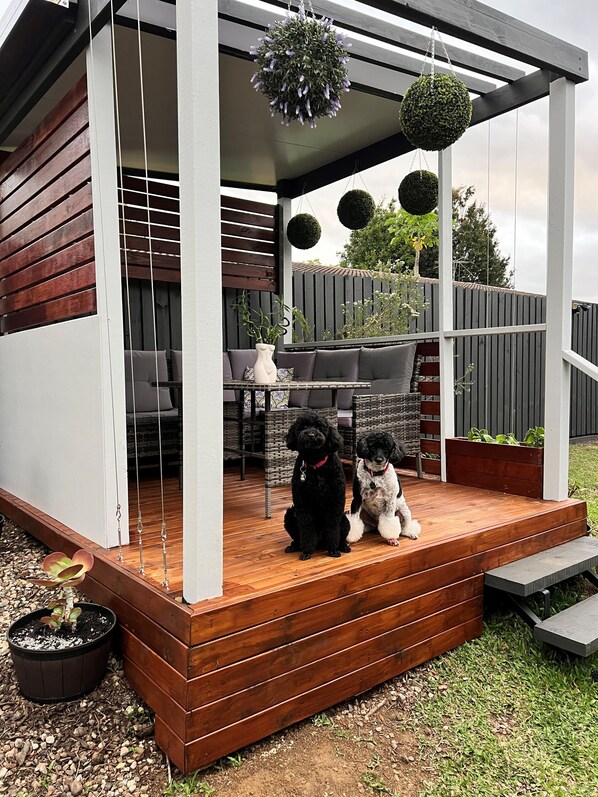 Un patio cubierto con terraza de madera, un espacio de descanso y dos perros.