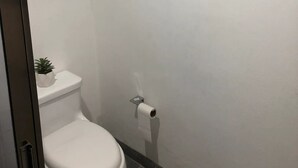 A bathroom with a white toilet, a towel hanging on a wall-mounted rack, and a small potted plant on the toilet tank. - CONDOS DR (Acapulco)