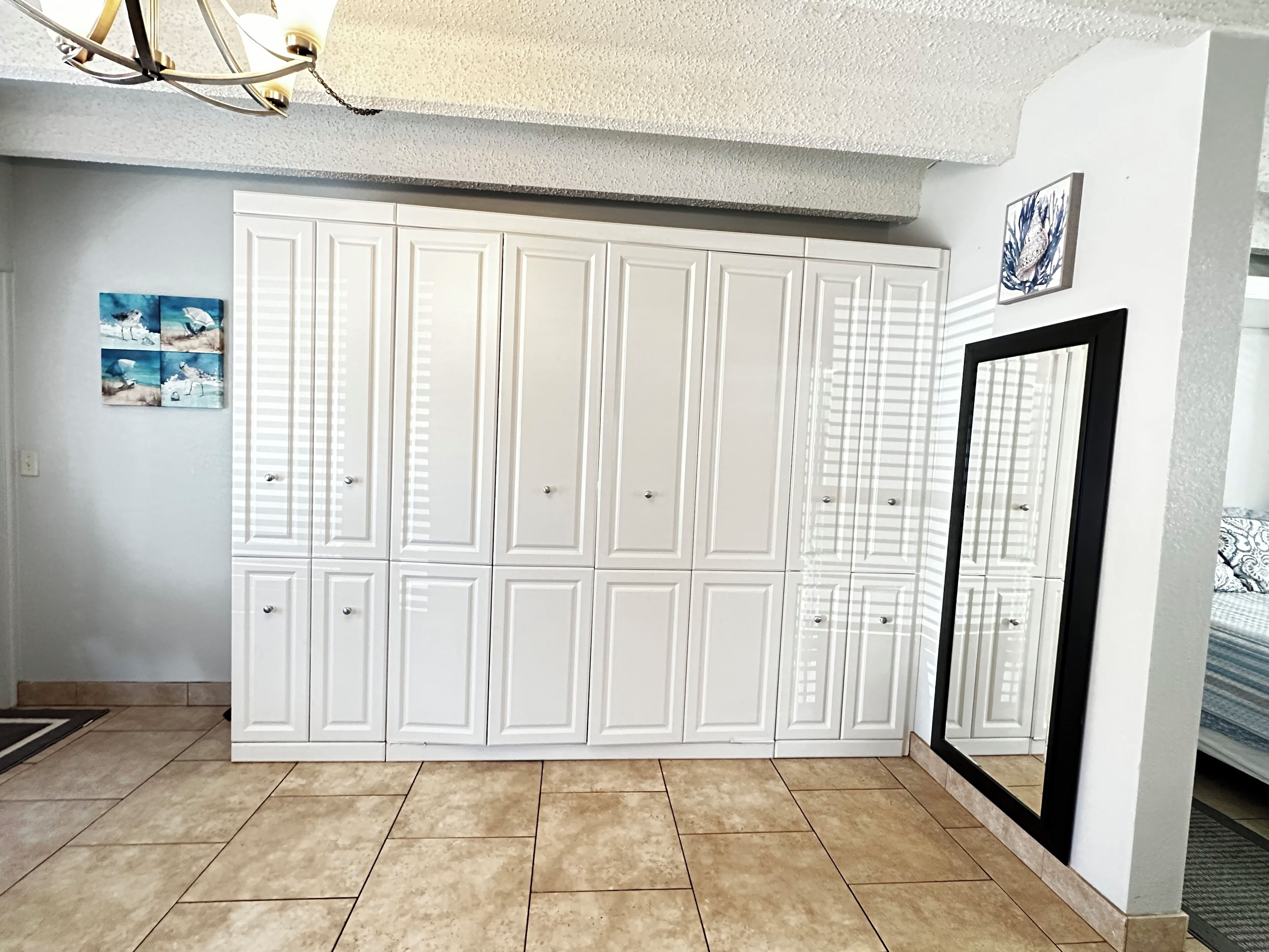A room with a large white wardrobe, a framed picture on the wall, and a mirror with a black frame.