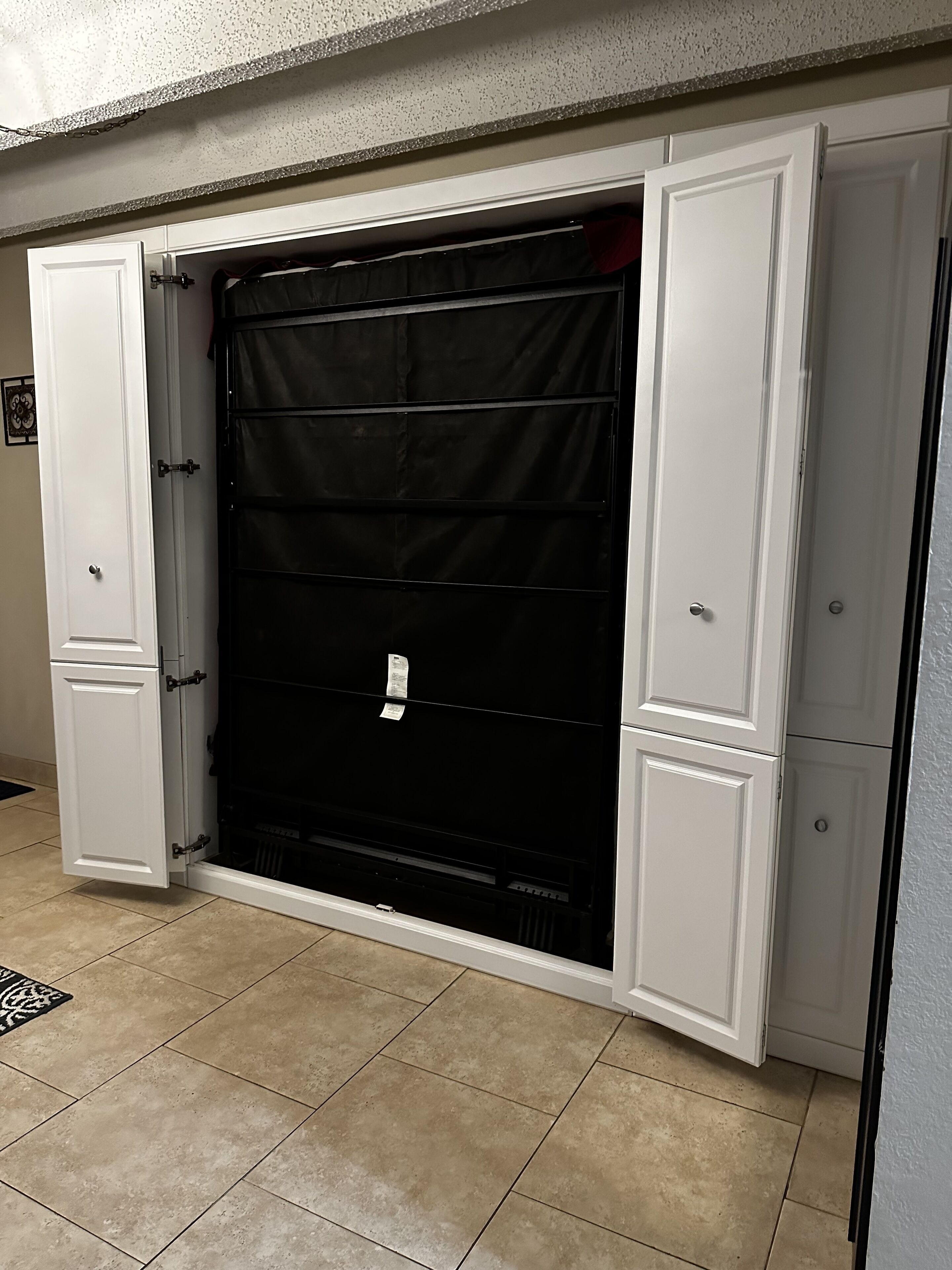 A room with a large black closet, white cabinets, and a tiled floor.