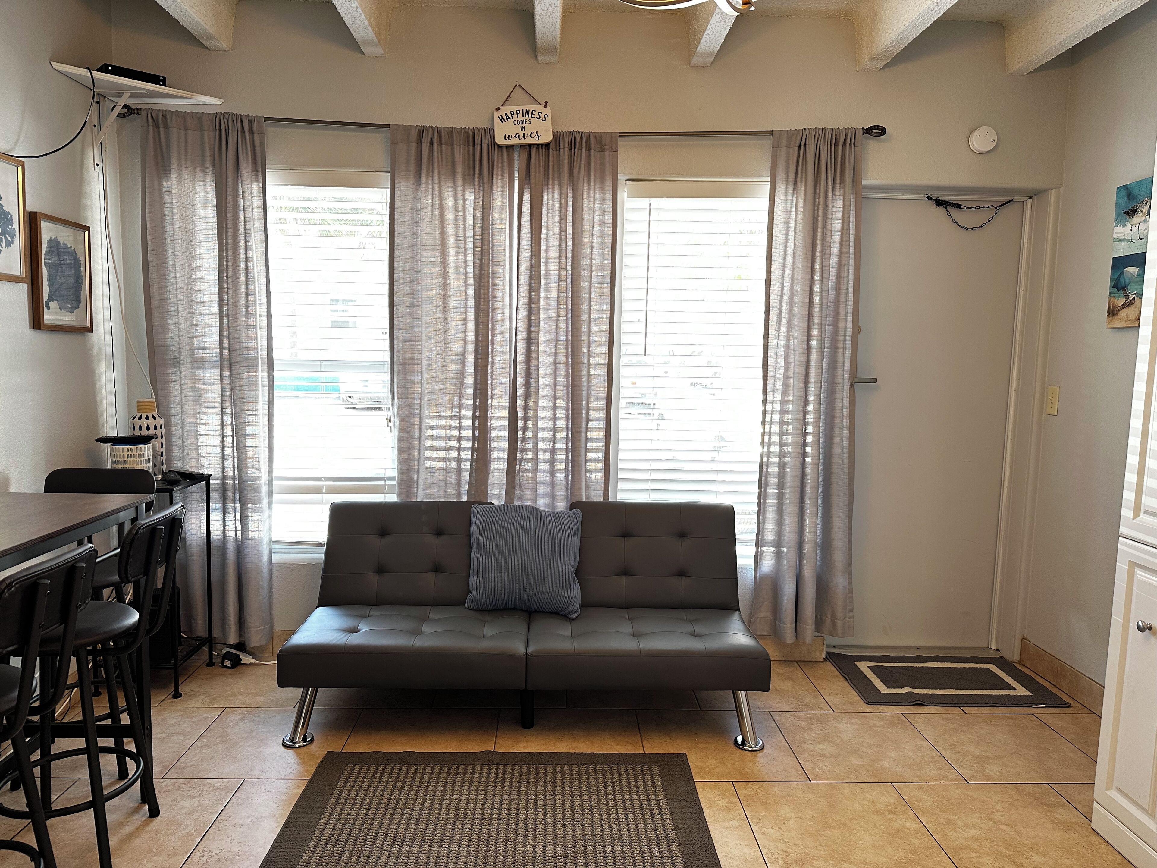 A living room with a sofa, a dining table with chairs, a rug, and a window with curtains.