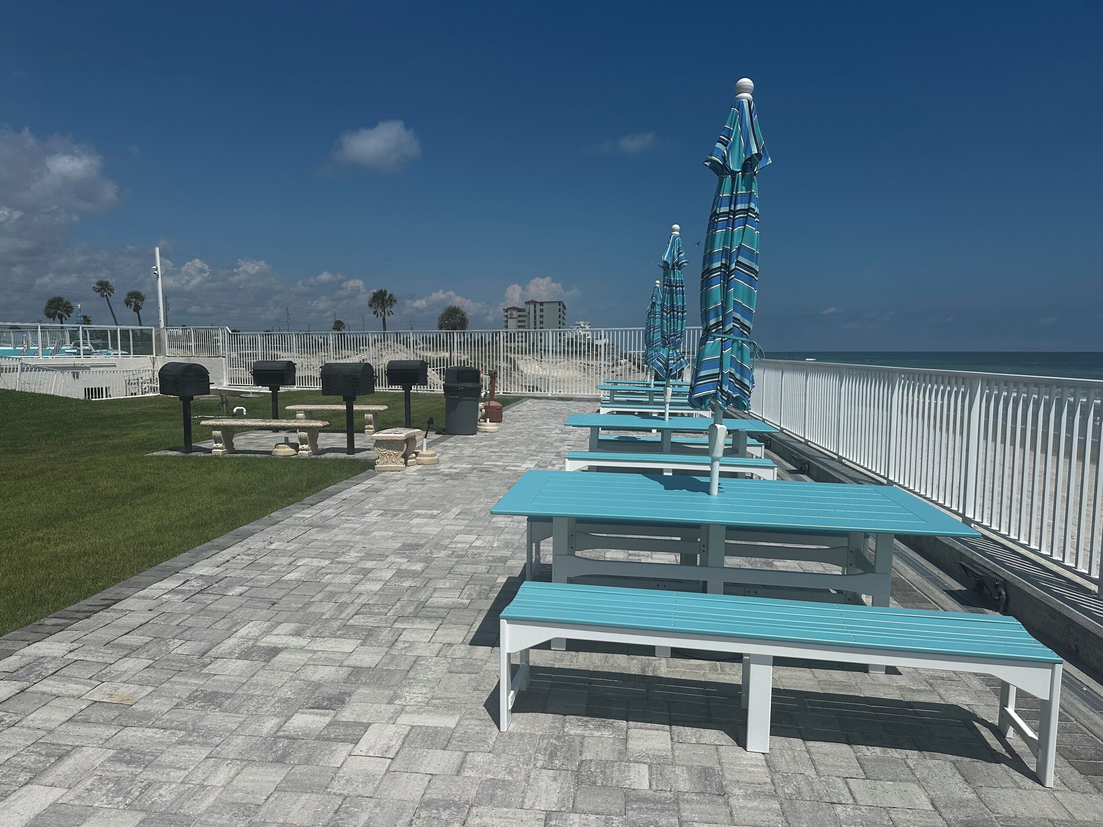 A seaside promenade with benches and umbrellas, a white fence, and a clear view of the ocean.