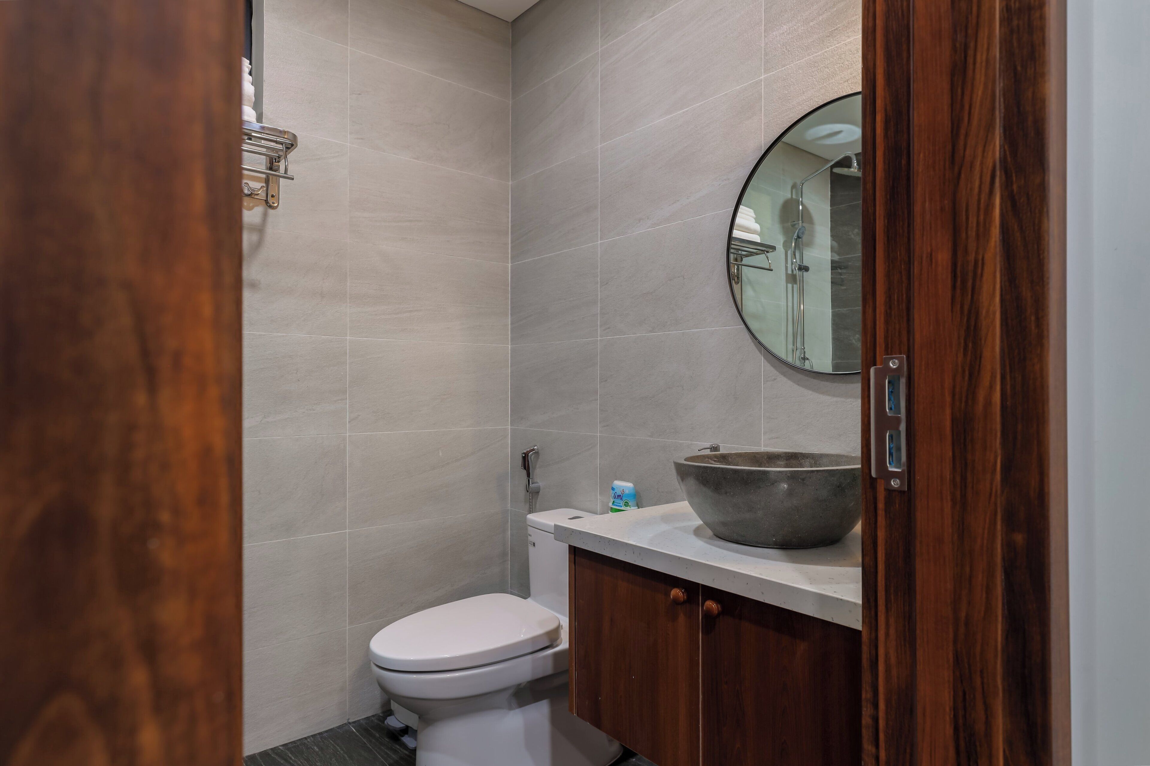 A bathroom with a toilet, a wooden cabinet, a large mirror, and a sink with a bowl.
