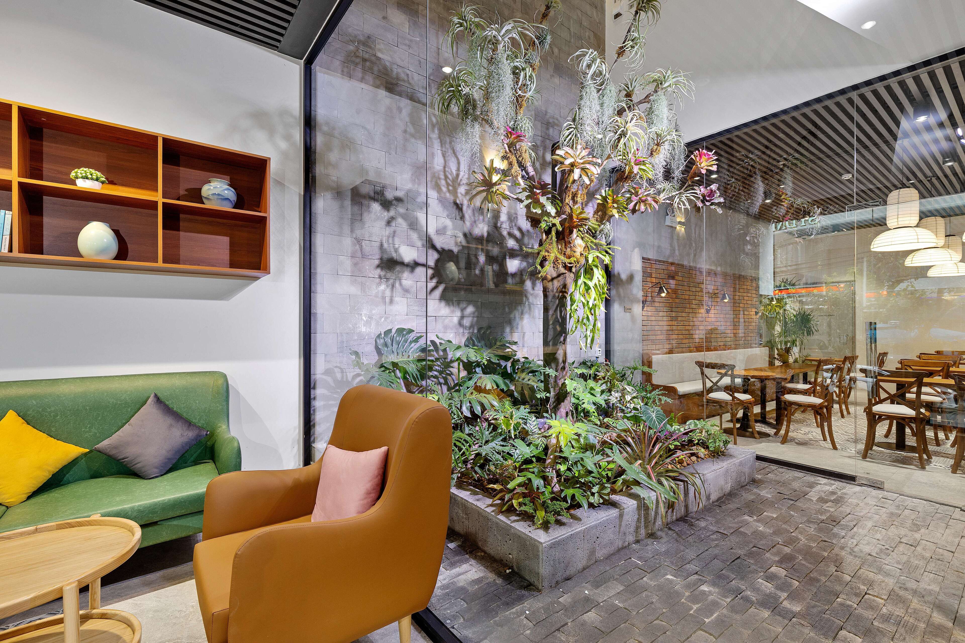 Um interior moderno com um sofá verde, uma cadeira de madeira, um arranjo de plantas e uma área de jantar com mesas e cadeiras.