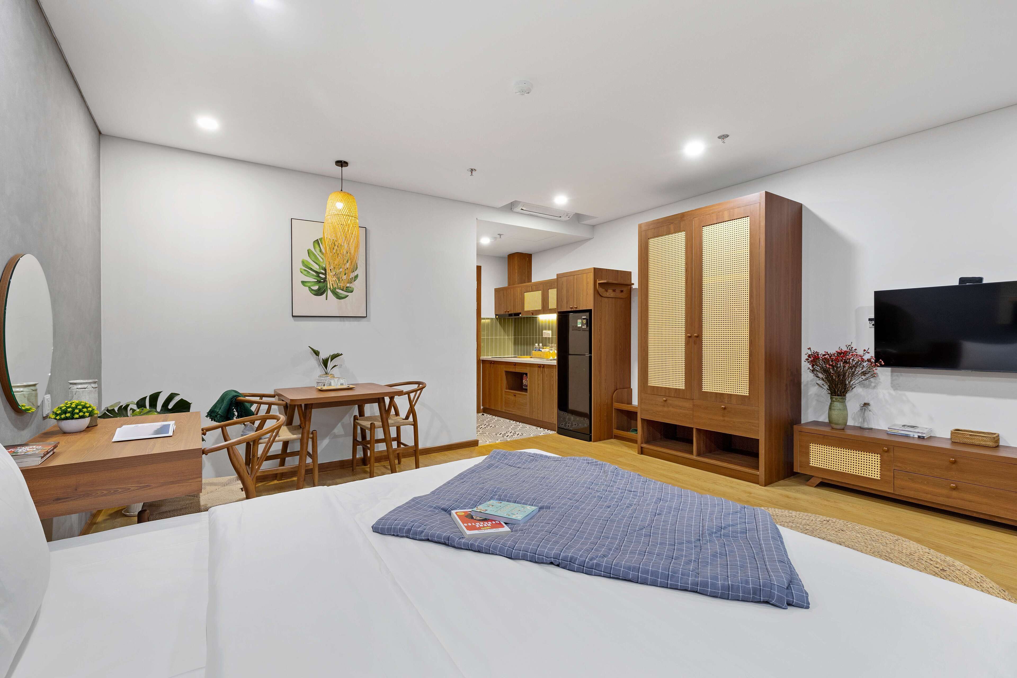 A modern hotel room with a bed, a desk, a chair, a dining area, and a TV.