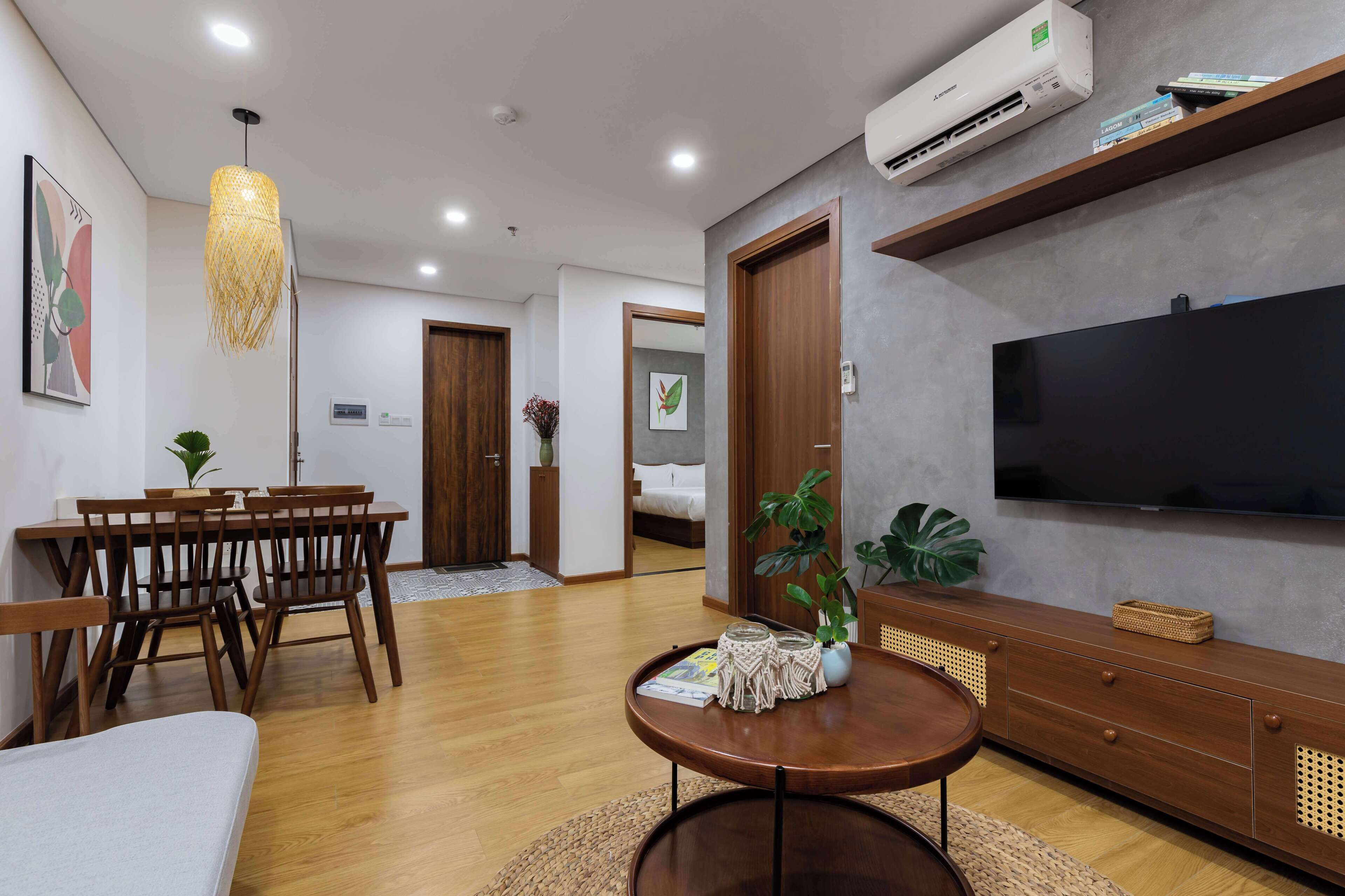 A modern living room with a dining area, a flat-screen TV, wooden furniture, and a large plant.