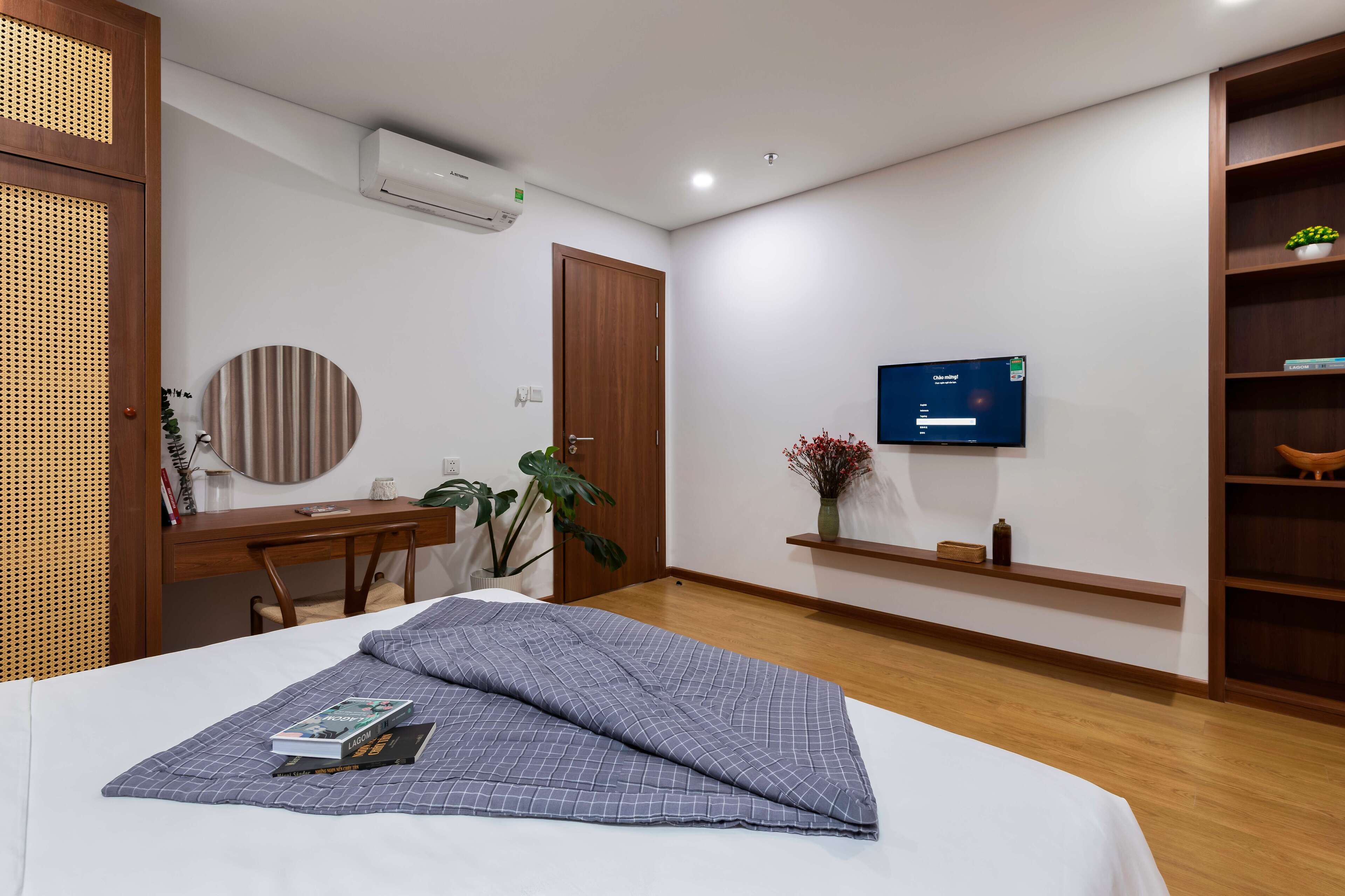 A modern hotel room with a bed, a desk, a chair, a television, and a bookshelf.