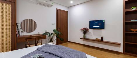 A modern hotel room with a bed, a desk, a chair, a television, and a bookshelf.
