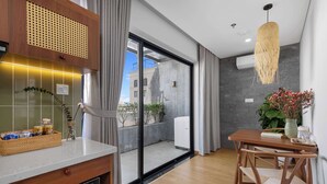 Eine moderne Küche mit Backofen, eine Essecke mit Holztisch und Stühlen sowie eine große Schiebeglasdoor zum Balkon.