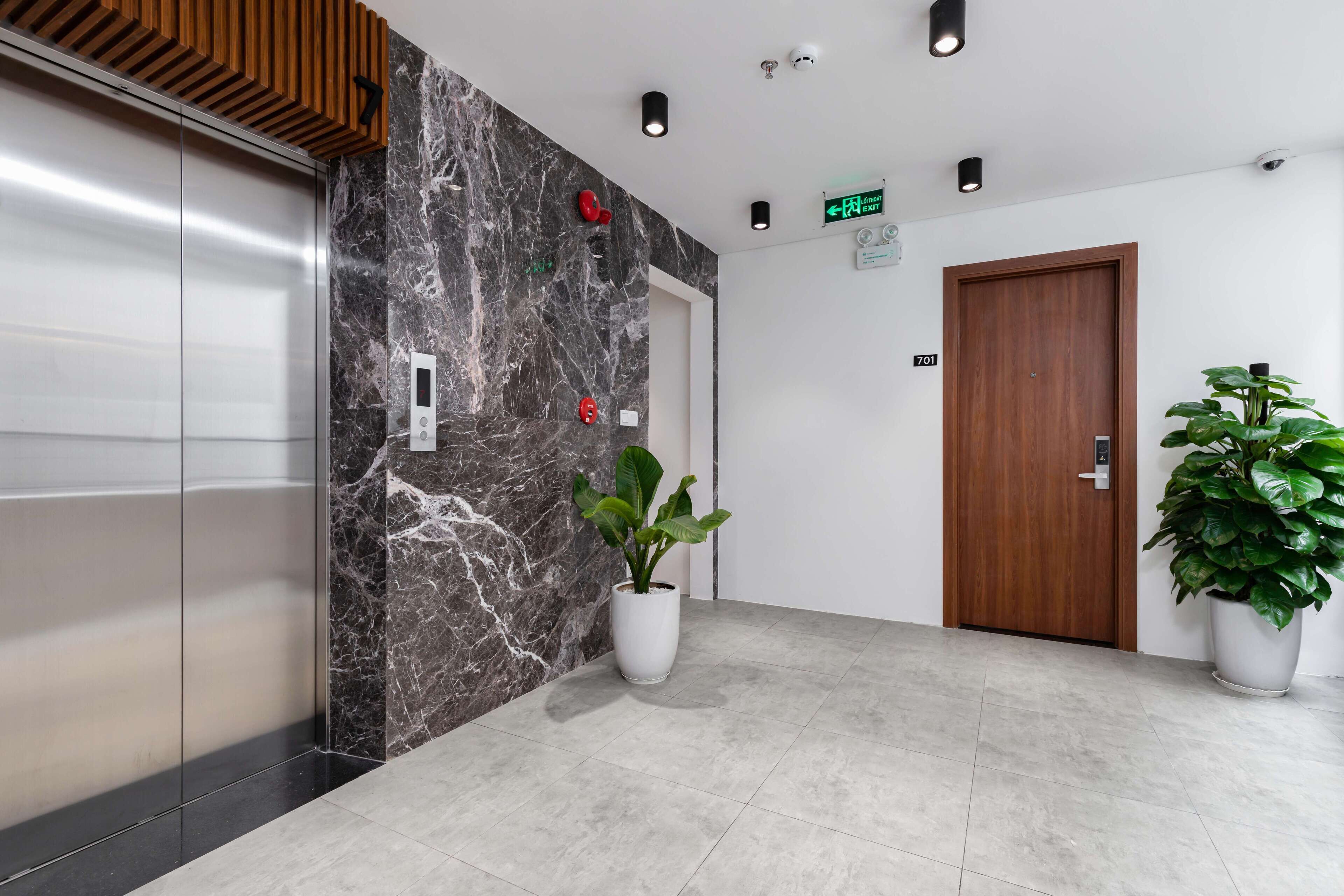 A modern lobby with a marble wall, a wooden door, and two potted plants.