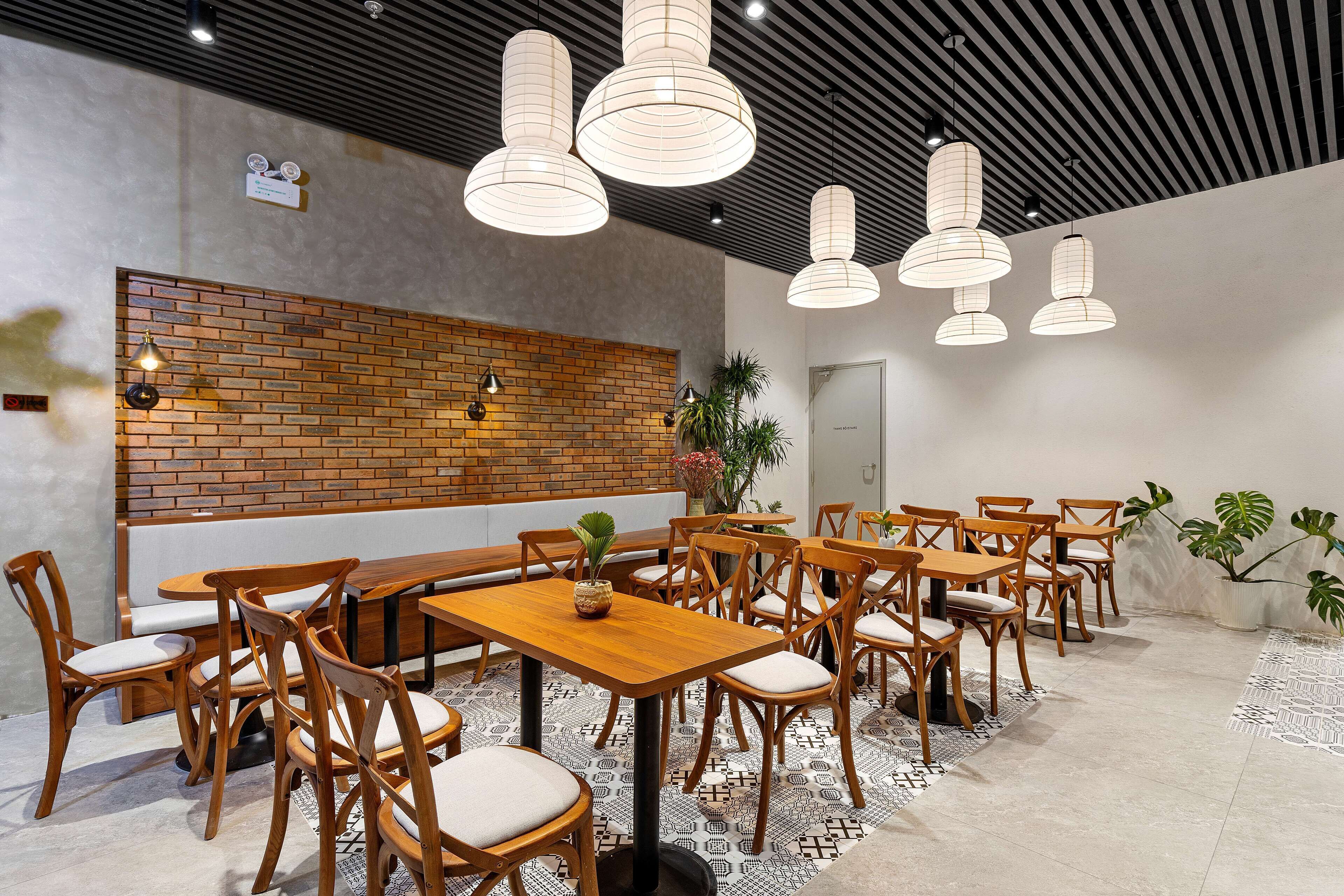 A modern dining area with wooden tables and chairs, a brick accent wall, and pendant lighting.