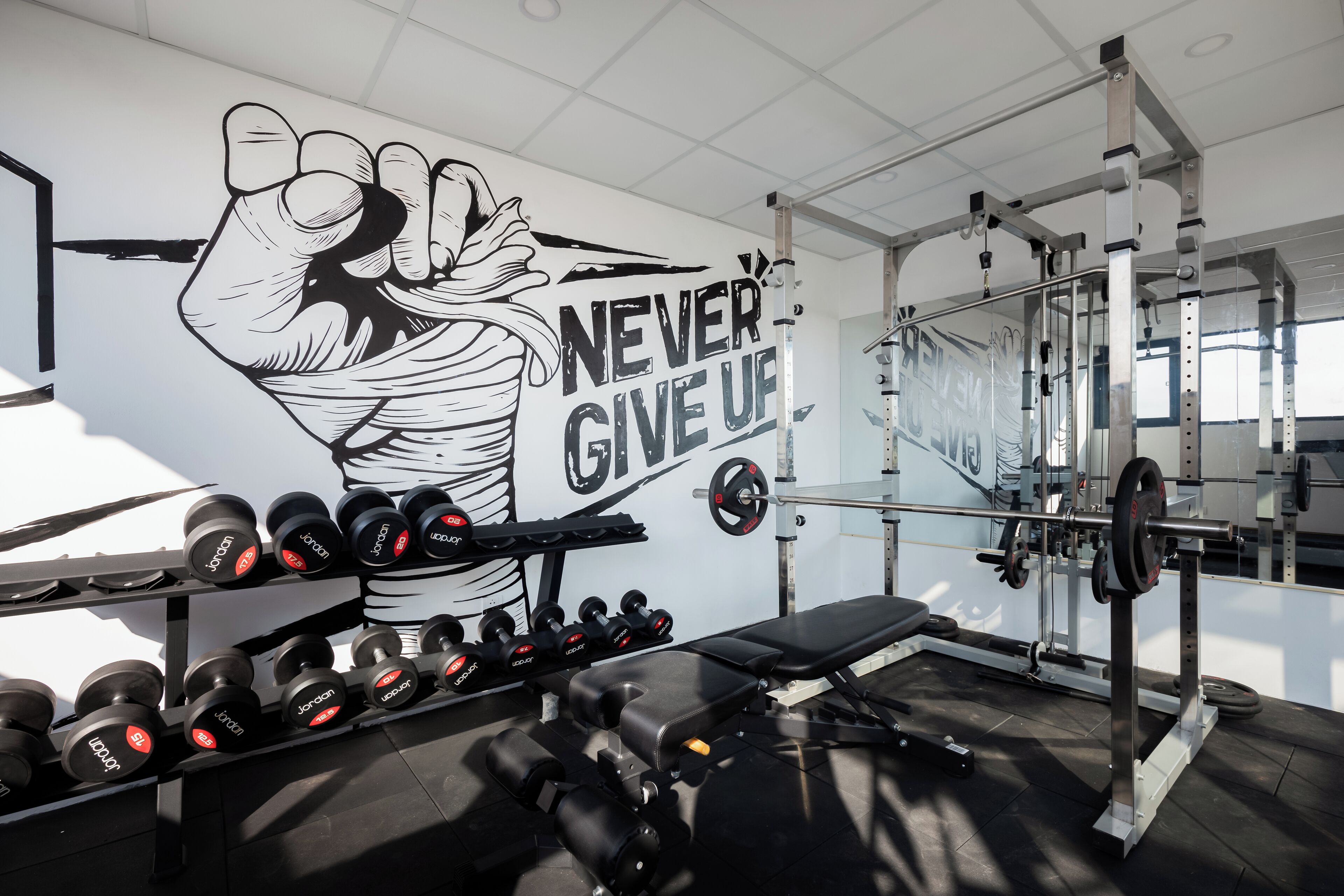 A gym with a motivational mural, dumbbells, a bench, and weightlifting equipment.