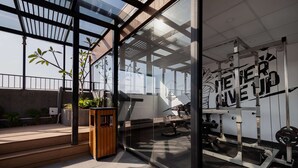 Ein modernes Fitnessstudio mit Glaswänden, einer Holzbank und einem motivierenden Zitat an der Wand.